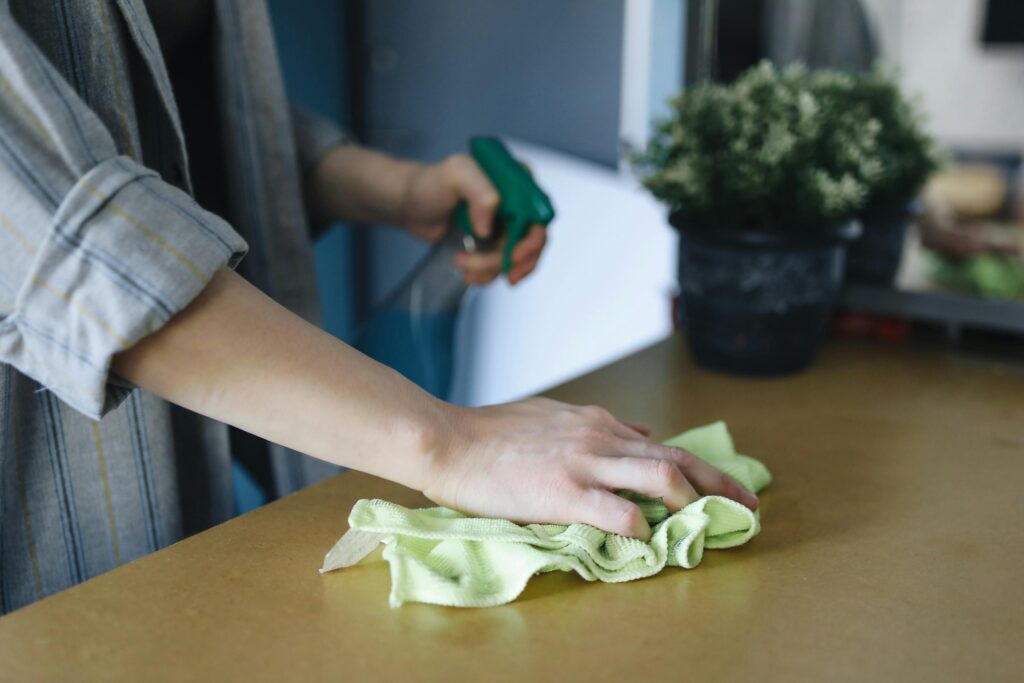 Pure Space Sustainable Cleaning Close-up of a woman wiping a table with a spray bottle and cloth indoors, symbolizing effective housekeeping.
