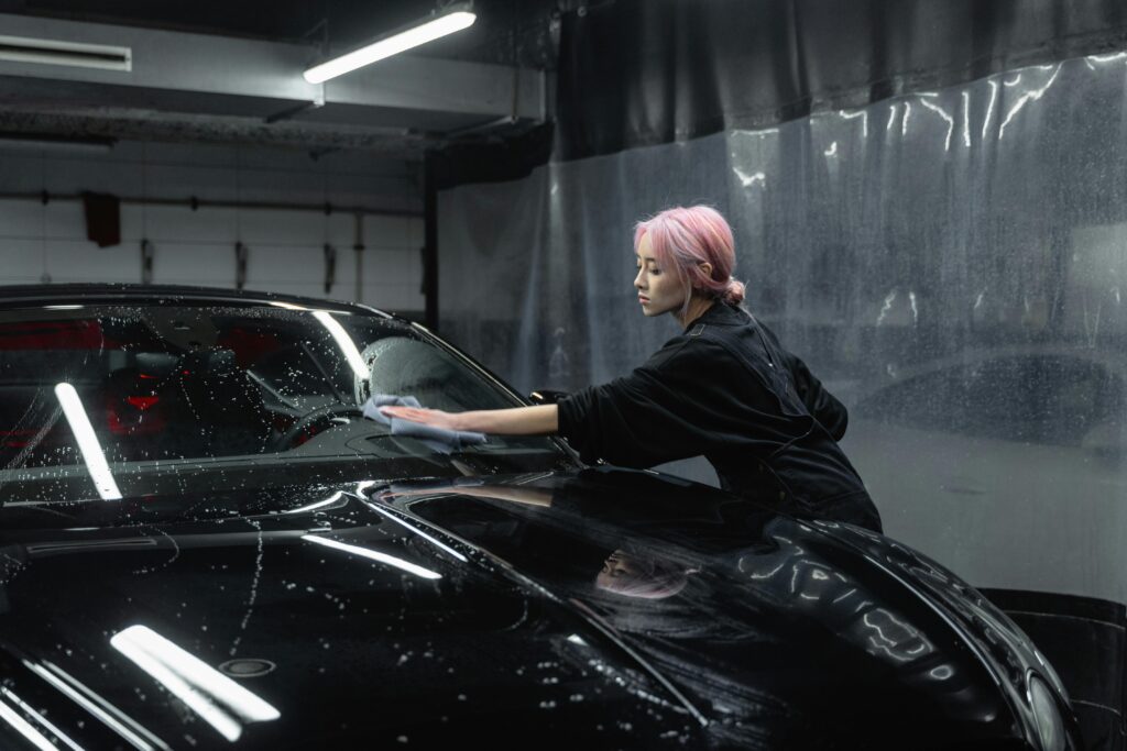 Green Car Wash: Eco-Friendly Mobile Detailing at Your Doorstep An adult woman with pink hair meticulously wiping down a black car at an indoor car wash.