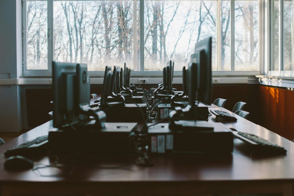 Office Cleaning An empty computer lab with multiple workstations and large windows during the daytime.