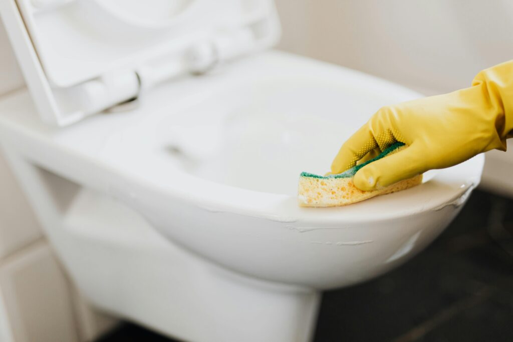 Bathroom Sanitization Close-up of a gloved hand using a sponge to clean a toilet, focusing on hygiene.