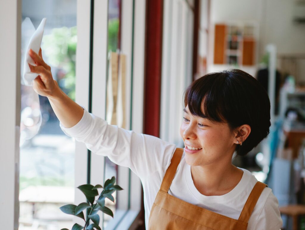 Post-Construction Cleaning Smiling woman in apron wipes glass window at a small business. Indoor shot.